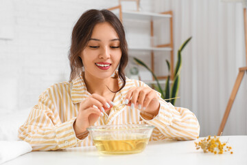 Young Asian woman preparing steam inhalation with herbs at table in bedroom
