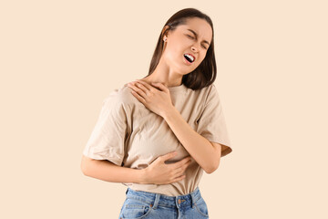Young woman suffering from shoulder pain on beige background