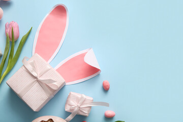 Easter eggs with tulip flower, gift boxes and paper bunny ears on blue background