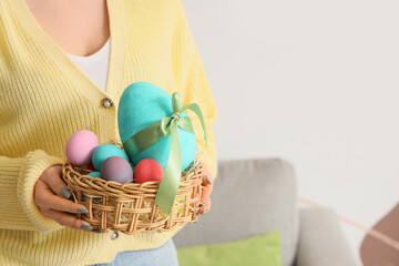 Woman with wicker basket of Easter eggs at home, closeup