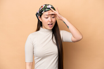 Young Chinese woman isolated on beige background doing surprise gesture while looking front