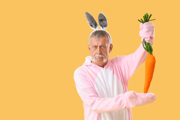 Naklejka premium Senior man in Easter bunny costume with plush carrot on yellow background