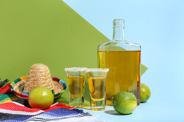 Bottle of tequila with shots and lime on color background