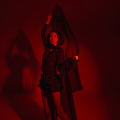 stylish Asian fashion woman in stylish shorts dancing with fabric canvases, photo in motion with artistic motion blur, red spotlight, totally red light