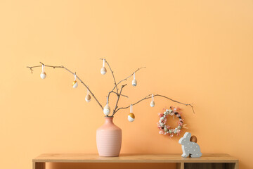Vase with tree branches and Easter eggs on shelf near beige wall