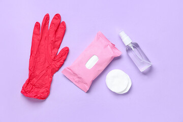 Rubber gloves with bottle of sanitizer and wet tissues pack on purple background
