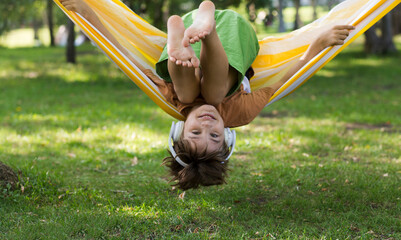 A portrait laughing preteen boy in headphones  listens to music looking at the camera  in a hammock...