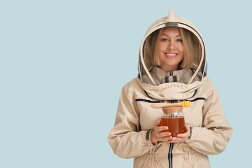 Female beekeeper with jar of sweet honey and dipper on blue background