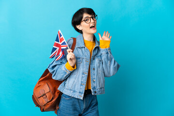 Woman holding an United Kingdom flag over isolated background saluting with hand with happy expression