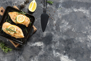 Frying pan with tasty chicken fillet, rosemary and lemon on grunge background