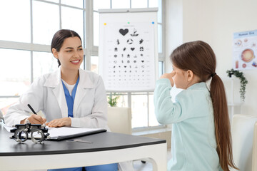 Fototapeta premium Female ophthalmologist working with little girl at table in clinic