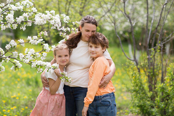 mom and two children  embrace amid flowering in garden in Spring .  stress relief. Spring awakening. Slow life. Enjoying the little things. Dreaming of spring.  banner