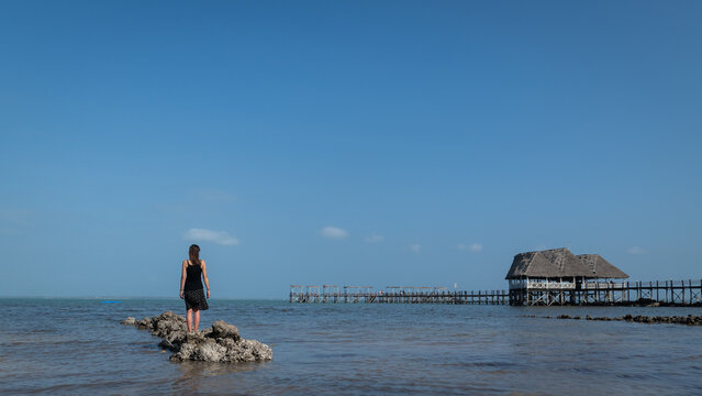 tropical background with woman standing on rocks of  beach near jetty in resort looking over the Indian Ocean in Zanzibar