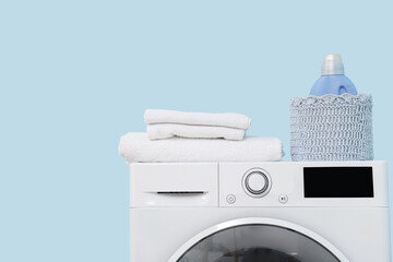 Modern washing machine with detergent and towels on blue background, closeup