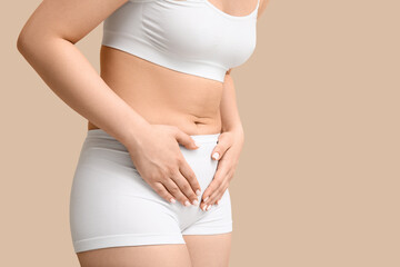 Young woman in underwear suffering from cystitis on beige background, closeup