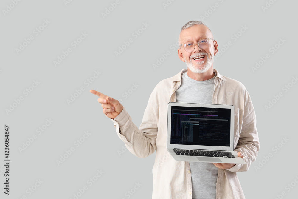 Poster mature programmer with laptop pointing at something on light background