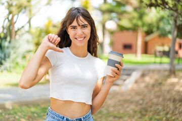 Young woman holding a take away coffee at outdoors proud and self-satisfied