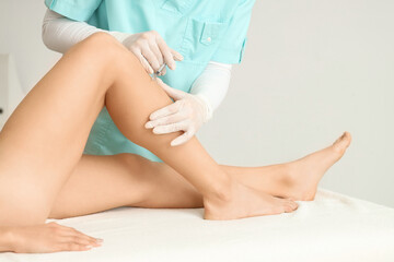 Young woman receiving injection in her leg on couch at cosmetologist's office