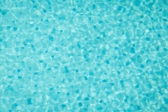 blue water background of swimming pool with pattern of small mosaic tiles and ripples