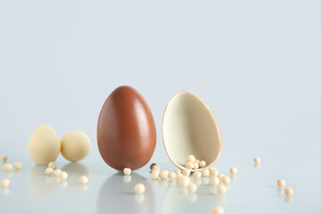Sweet chocolate eggs with scattered candies on grey background