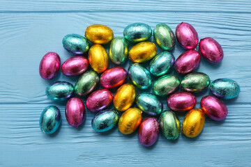 Many chocolate Easter eggs in foil on blue wooden background