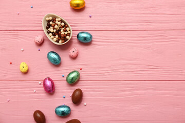 Chocolate Easter eggs with candies on pink wooden background