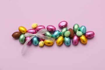 Obraz premium Chocolate Easter eggs in foil with bow on lilac background