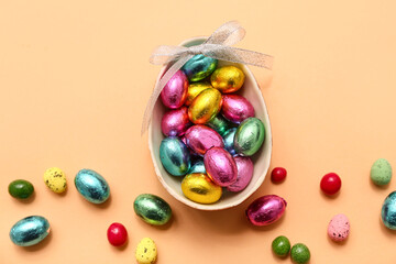 Chocolate Easter eggs in foil with bow and candies on beige background