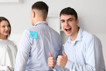 Young colleagues and man with sticky paper on his back in office. April Fools' Day celebration