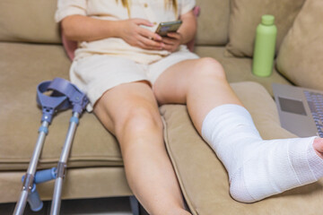 Fototapeta premium Resting with an injured leg, working from home with a laptop and smartphone, embracing self-care and recovery