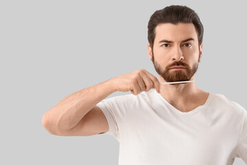 Handsome young man combing his beard on grey background