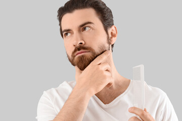 Handsome young man combing his beard on grey background