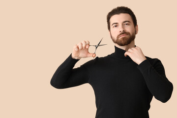 Bearded young man with scissors on beige background