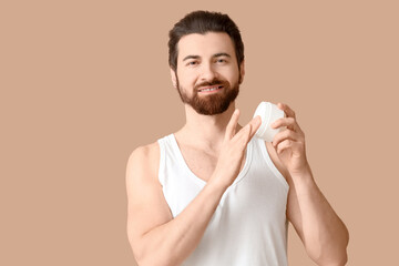 Bearded young man with skin care cream on beige background
