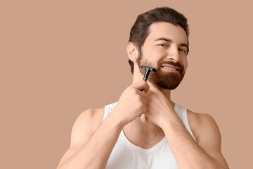 Handsome young man shaving his beard with razor on beige background
