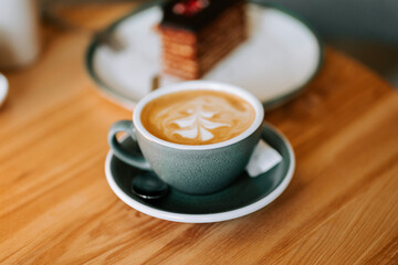 Warm latte art on a wooden table beside a layered dessert in a cozy cafe setting during the afternoon