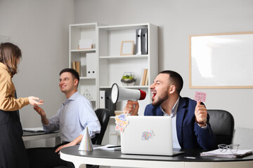 Young man with paper shouting into megaphone in office. April Fools' Day celebration