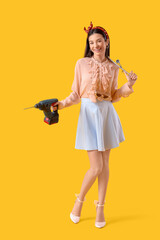 Young pin-up woman with electric drill and cross wrench on yellow background. Women's History Month