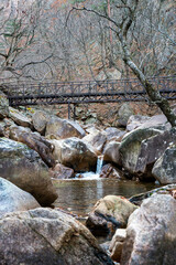 가을 산속의 바위 사이 작은 폭포가 떨어지는 호수와 철제 다리