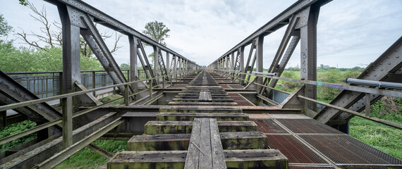 Diminishing view of an abandoned rusty railroad bridge made of steel framework, lost place