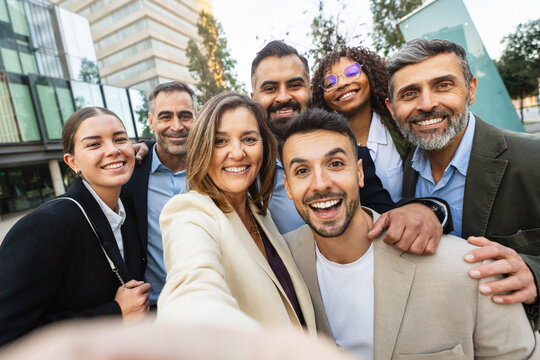 Group of cheerful multiethnic business people taking a selfie with mobile phone app in front of their modern office building