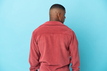 Young latin man isolated on blue background in back position and looking side