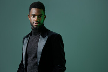 Confident young man in stylish black attire posing against a vibrant green backdrop