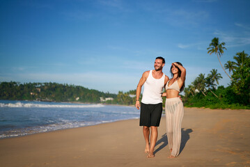 Happy couple strolls on sandy beach at tropical destination. Romantic walk, shoreline embrace,...