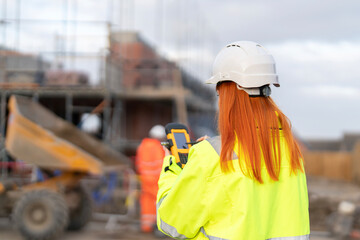 Female Construction project manager using a digital device to monitor progress at a building site under overcast skies in the afternoon