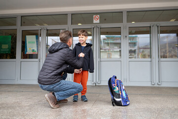 Father helps son dress near school, showing parental care and pickup.