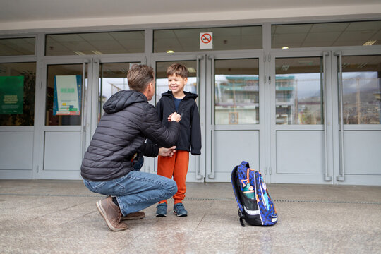 Father helps son dress near school, showing parental care and pickup.