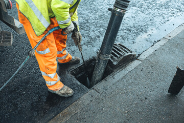 Workers conduct maintenance on drainage system on  city street during daytime