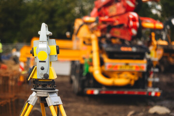 Fototapeta premium Surveying equipment positioned at construction site with heavy machinery and workers engaged in various activities during daylight