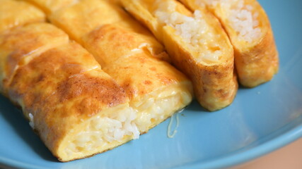 roll omelette stuffed with chesse and rice on blue plate, delicious food in the morning